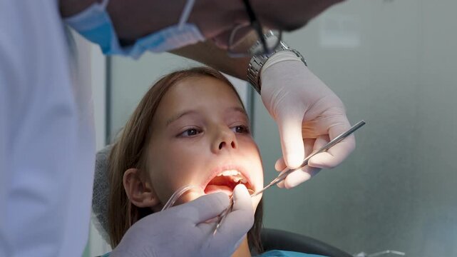 Pediatric dentist examining teeth with mirror and probe for young girl