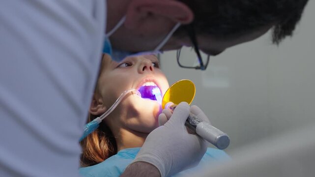 Pediatric dentist using UV curing light lamp on tooth filling for young girl.