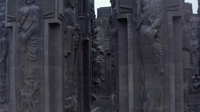 Aerial drone retreats between the Chronicle of Georgia pillars in Tbilisi, revealing monumental reliefs and the city beyond for religious history, cultural education, tourism, documentary production