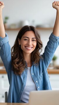 Happy young woman celebrating success with raised arms and bright smile. Positive emotions and achievement captured in a modern indoor setting with natural light
