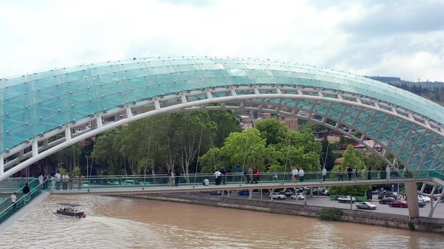 Bridge of Peace spans river-level aerial view across the Mtkvari in central Tbilisi, connecting Rike Park and Old Town for urban tourism, contemporary architecture and destination promotion.