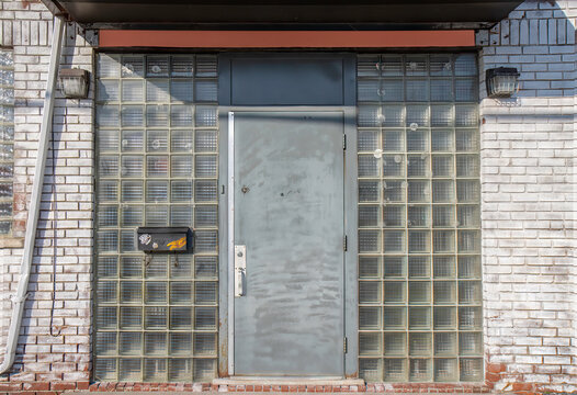 Steel door building entrance door with glass blocks side windows, partial roof over entrance, black mailbox, dirty white brick walls, nobody