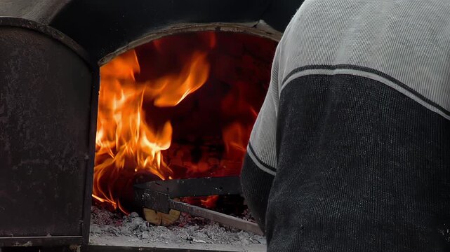 Person Adding Logs with Metal Tool into Flaming Wood Burning Oven - 4K