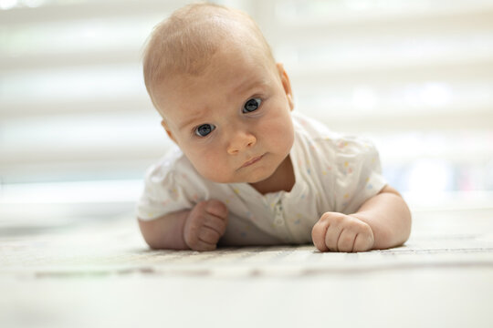 Adorable infant lying on tummy on a rug, looking curiously at the camera during tummy time at home.