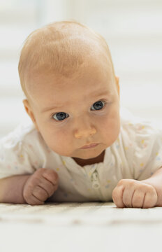 Vertical photo of adorable infant lying on tummy on a rug, looking curiously at the camera during tummy time at home.