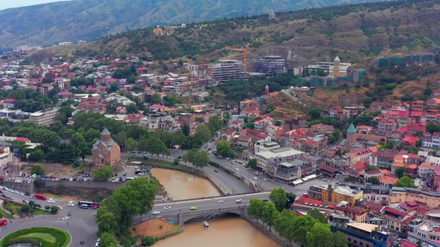 Central Tbilisi follows aerial view along the Mtkvari River, Metekhi Bridge and historic districts, supporting city tourism, transport planning, riverfront geography and Georgian travel media.