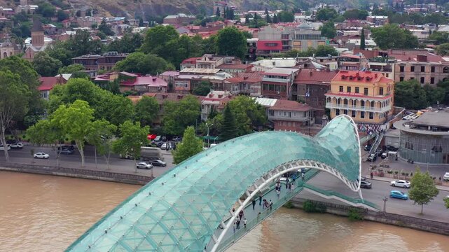 Bridge of Peace spans overhead aerial view across the Mtkvari River in central Tbilisi, supporting architecture tourism, pedestrian mobility, riverfront branding and Georgian destination campaigns.