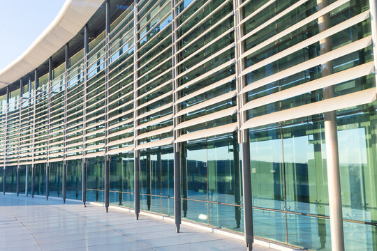Curved exterior glass facade of a modern corporate office building featuring horizontal metal sun louvers and steel support columns reflecting sunlight.