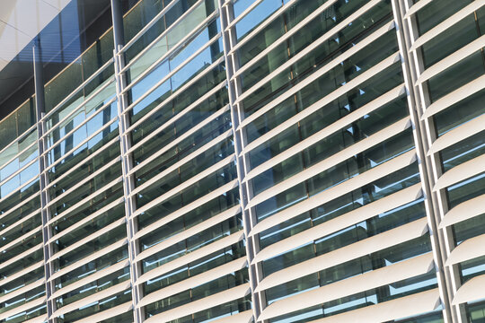 Curved exterior glass facade of a modern corporate office building featuring horizontal metal sun louvers and steel support columns reflecting sunlight.