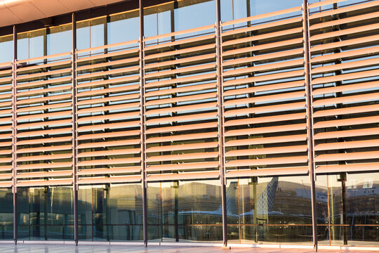 Curved exterior glass facade of a modern corporate office building featuring horizontal metal sun louvers and steel support columns reflecting sunlight.