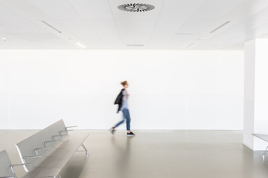 Motion blur of woman walking at contemporary white empty hallway.