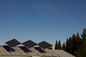 Fototapeta premium Three photovoltaic solar panels installed on the metal roof of a mountain building under a clear blue sky. The renewable energy system generates clean electricity in a remote alpine environment, 