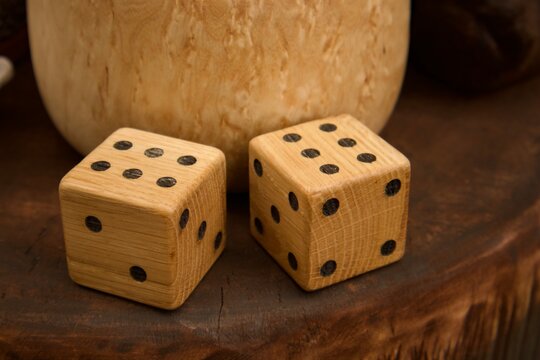 Two handcrafted wooden dice resting on a rustic wooden surface with a natural wooden vessel in the background. The warm tones, handcrafted craftsmanship, and traditional game accessories create 