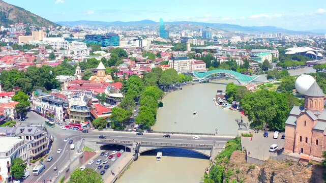Metekhi Bridge advances in aerial view across the Mtkvari River beside historic Tbilisi districts, supporting transport planning, urban tourism, waterfront geography and regional travel media.