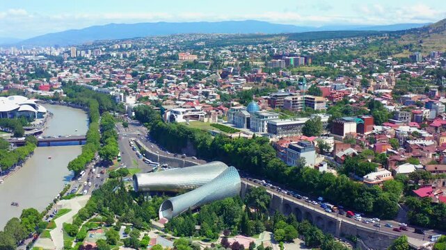 Central Tbilisi advances in aerial view above Rike Park, the Mtkvari River and cultural architecture, supporting city branding, urban planning, tourism campaigns and regional geography media.