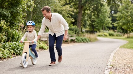 Fototapeta premium Father helping child ride balance bike in park during summer 