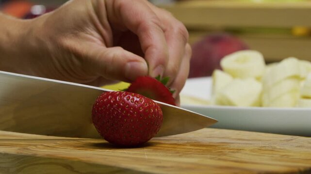 Slow motion shot of sharp knife slicing up single strawberry