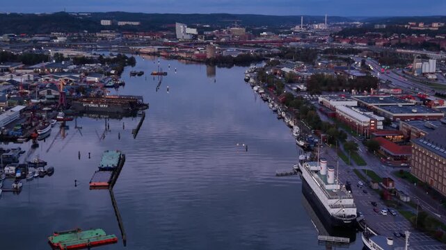 Gothenburg, Vastra Gotaland County - 16 July 2026: Aerial view of Gota alv river flowing through the industrial harbor area of Gothenburg with moored ships and urban buildings at dusk.