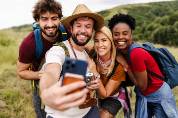 Obraz premium A group of four friends joyfully poses for a selfie in a scenic outdoor setting, surrounded by lush greenery, capturing a moment of fun and camaraderie.