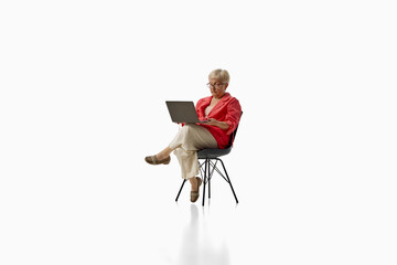 Fototapeta premium Senior woman working on laptop while seated isolated on white background. Concept of digital inclusion, remote work, lifelong learning.