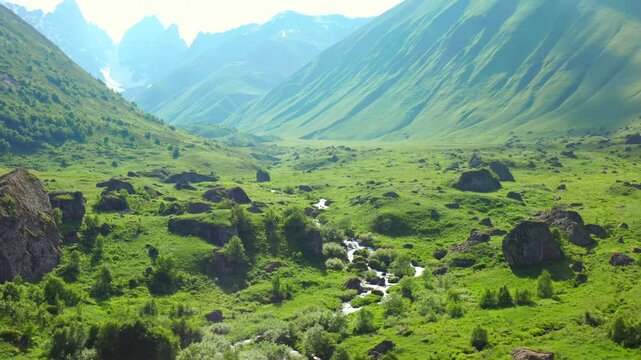 Roshka mountain creek curves beneath aerial view across a broad green valley and scattered boulders, supporting watershed mapping, trekking tourism, environmental education, Georgian landscape media