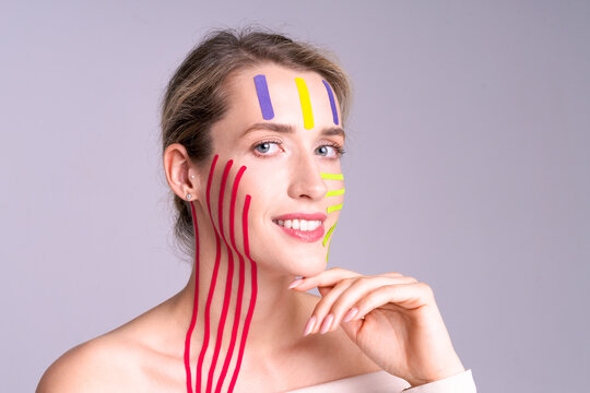 Woman gently touches her face with red tape lines on her skin, symbolizing skin care, tightening and freshness, studio shooting