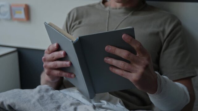 Unknown male soldier with bandaged arm lying in hospital bed and reading book. Video for veteran rehabilitation and healthcare services marketing