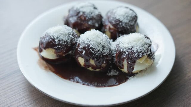 Close-up of profiteroles with chocolate sauce on white plate