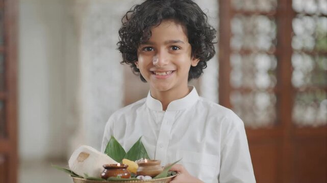 Happy Indian boy in white kurta holding a traditional puja thali
