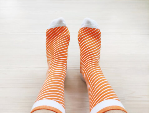 Feet wearing soft knitted patterned socks on a light wooden floor. Cozy domestic shot from a side view, concept of comfort, warmth, relaxation, leisure, and casual home fashion