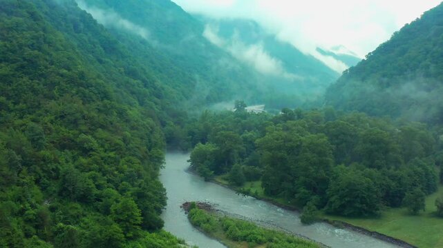 Aragvi River curves through aerial view between dense woodland and mist-covered mountains in Georgia, supporting nature tourism, riparian ecology, watershed education and destination marketing.
