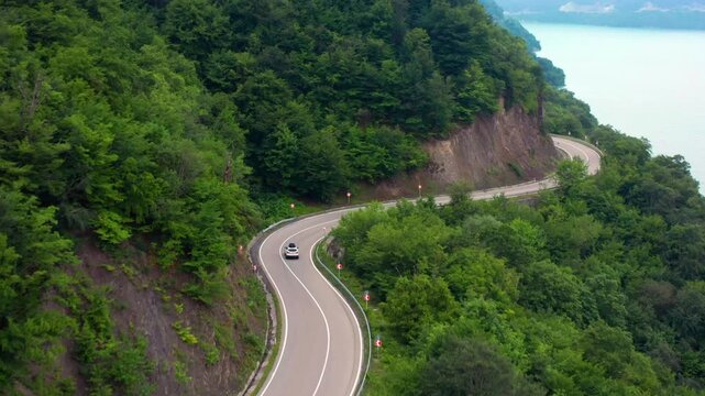 Aerial drone flies forward above a winding highway near Zhinvali Reservoir in Georgia, tracing a sharp bend through dense forest for scenic driving, road infrastructure, tourism and travel promotion.