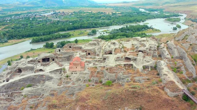 Uplistsikhe complex fills high-angle aerial view above carved terraces and the Mtkvari River valley, supporting heritage tourism, archaeology mapping, museum media and Georgian travel campaigns.