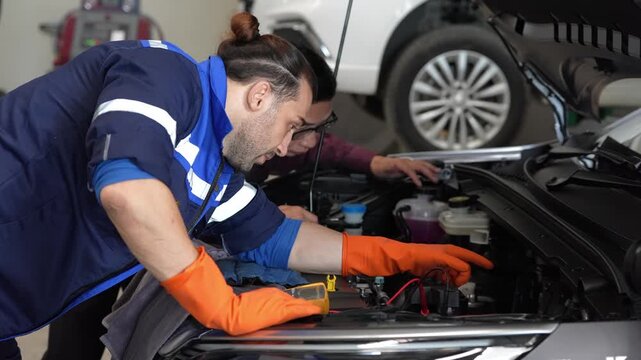 Mechanic car engine repair service garage inspection maintenance technician team under open hood testing battery wiring, orange glove diagnostic work in workshop