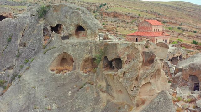 Uplistsikhe caves spread through oblique aerial view beneath a hilltop church and eroded sandstone walls, supporting cultural tourism, sacred heritage and Georgian archaeology documentaries.