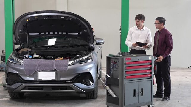 Car mechanic inspection and repair in service garage, diagnostic maintenance technician discussing engine check on tablet, two staff examining open hood beside toolbox and scan tool