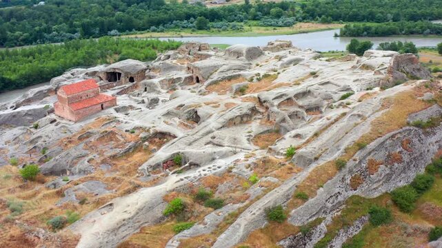 Drone orbits above Uplistsikhe rock city in Georgia, revealing cave chambers, a hilltop church and river landscape for cultural tourism, historical documentaries and archaeology research projects.