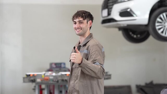 Mechanic automotive workshop car service repair maintenance gesture smiling technician in uniform giving thumbs up beside vehicle lift on hoist inside garage, auto repair concept with copy space