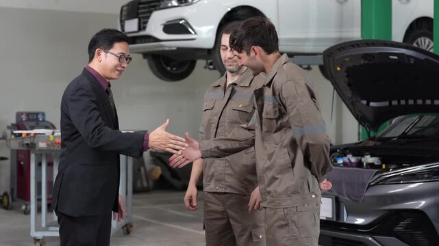 Car mechanic handshake with customer in garage service, repair and maintenance inspection meeting, technician team discusses estimate beside open hood and car lift, businessman trust partnership