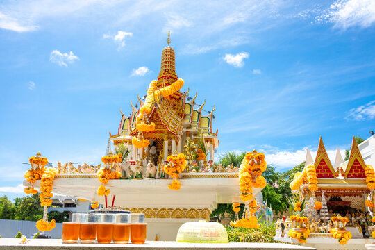 Thai spirit house shrine decorated with marigold garlands and offerings under blue sky in Thailand