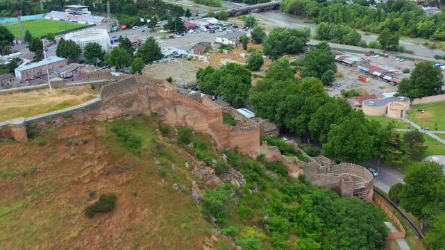 Aerial drone circles Gori Fortress in Georgia, revealing hilltop defensive walls, surrounding streets and urban greenery for heritage tourism, historic architecture and city destination promotion.