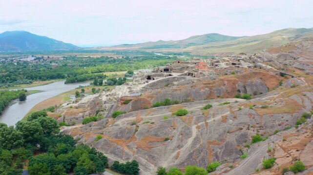 Aerial drone descends toward Uplistsikhe cave city in Georgia, revealing rock-cut chambers, pale terraces and the Kura River valley for archaeology, heritage tourism and educational projects.