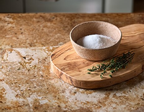 worn olive wood cutting board with ceramic bowl of coarse salt and fresh thyme sprig on honed travertine countertop in tuscan revival kitchen