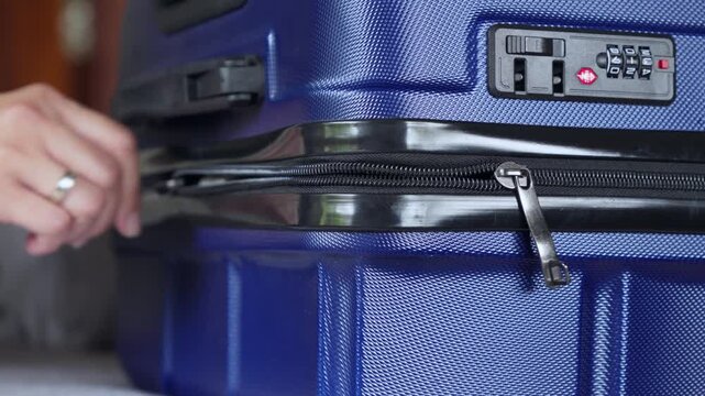 Hand gently zips blue suitcase with analog lock, vacation concept