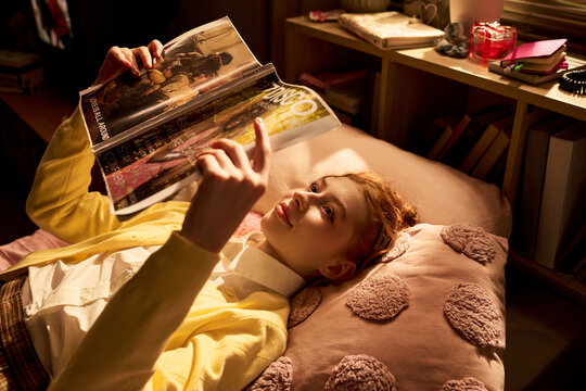 Teenage girl lying on bed and reading fashion magazine, browsing style content during leisure time. Useful for youth lifestyle, media consumption, trend marketing campaigns