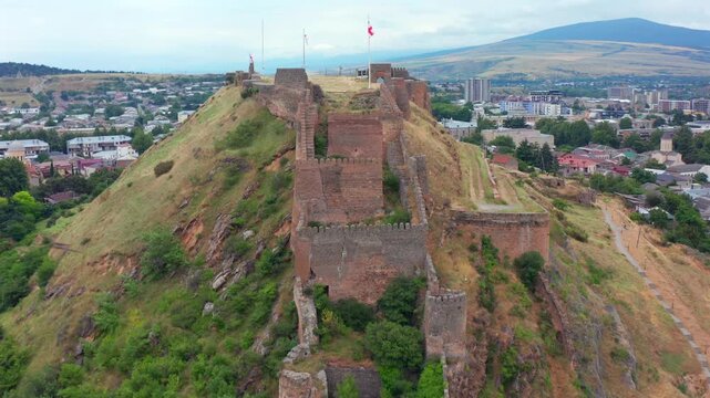 Drone retreats above Gori Fortress in Georgia, widening across hilltop walls, city districts and surrounding mountains for heritage tourism, historical media, urban geography and destination promotion