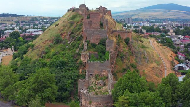 Drone flies forward toward Gori Fortress in Georgia, approaching defensive walls on a rocky hill above the city for heritage tourism, medieval history, architecture and landmark promotion media.
