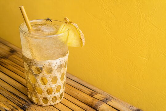 Tropical pineapple cocktail in a woven glass on yellow background