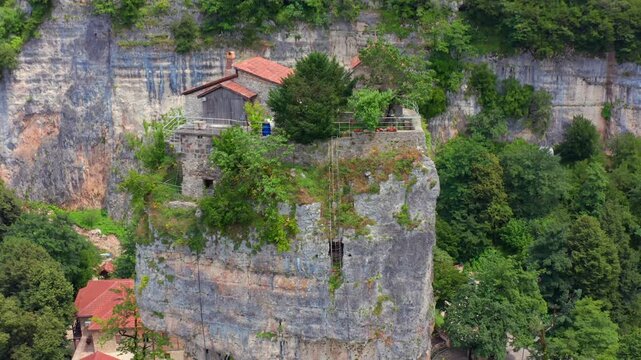 Katskhi Pillar rises in aerial view above monastery roofs and forested limestone cliffs in Imereti, supporting religious tourism, Georgian heritage media and remote landmark travel promotion.