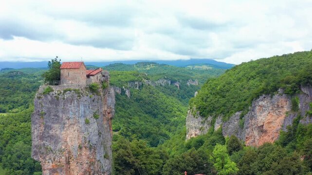 Katskhi Pillar anchors aerial view above wooded ravines and distant Imereti hills, supporting Georgian tourism, sacred heritage, rural geography and iconic landmark destination travel campaigns.